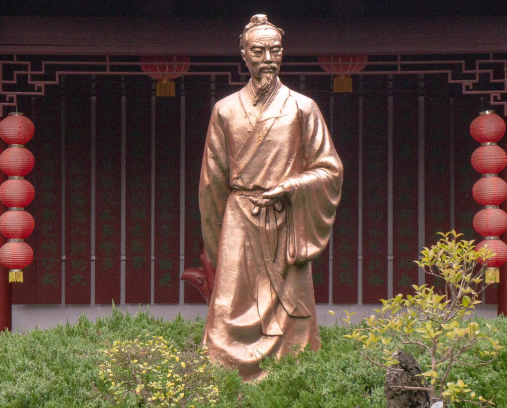 Golden statue of Lu Yu standing in a garden with tea bushes nearby